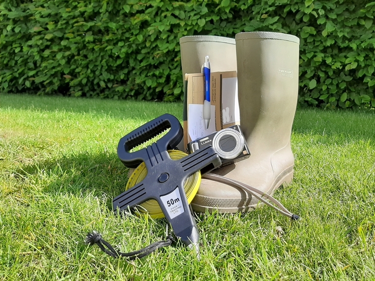 Gummistiefel mit Maßband vor einer Hecke