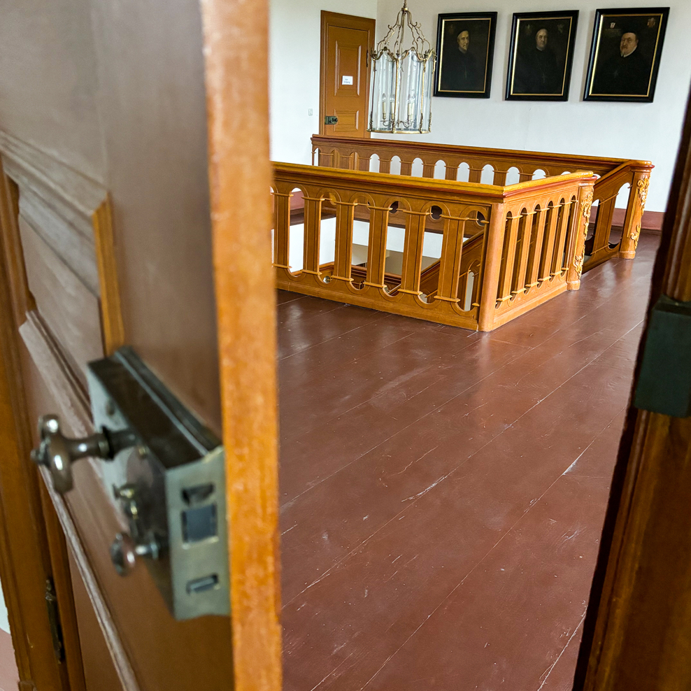 Blick durch eine spaltweit geöffnete Tür in das alte Treppenhaus